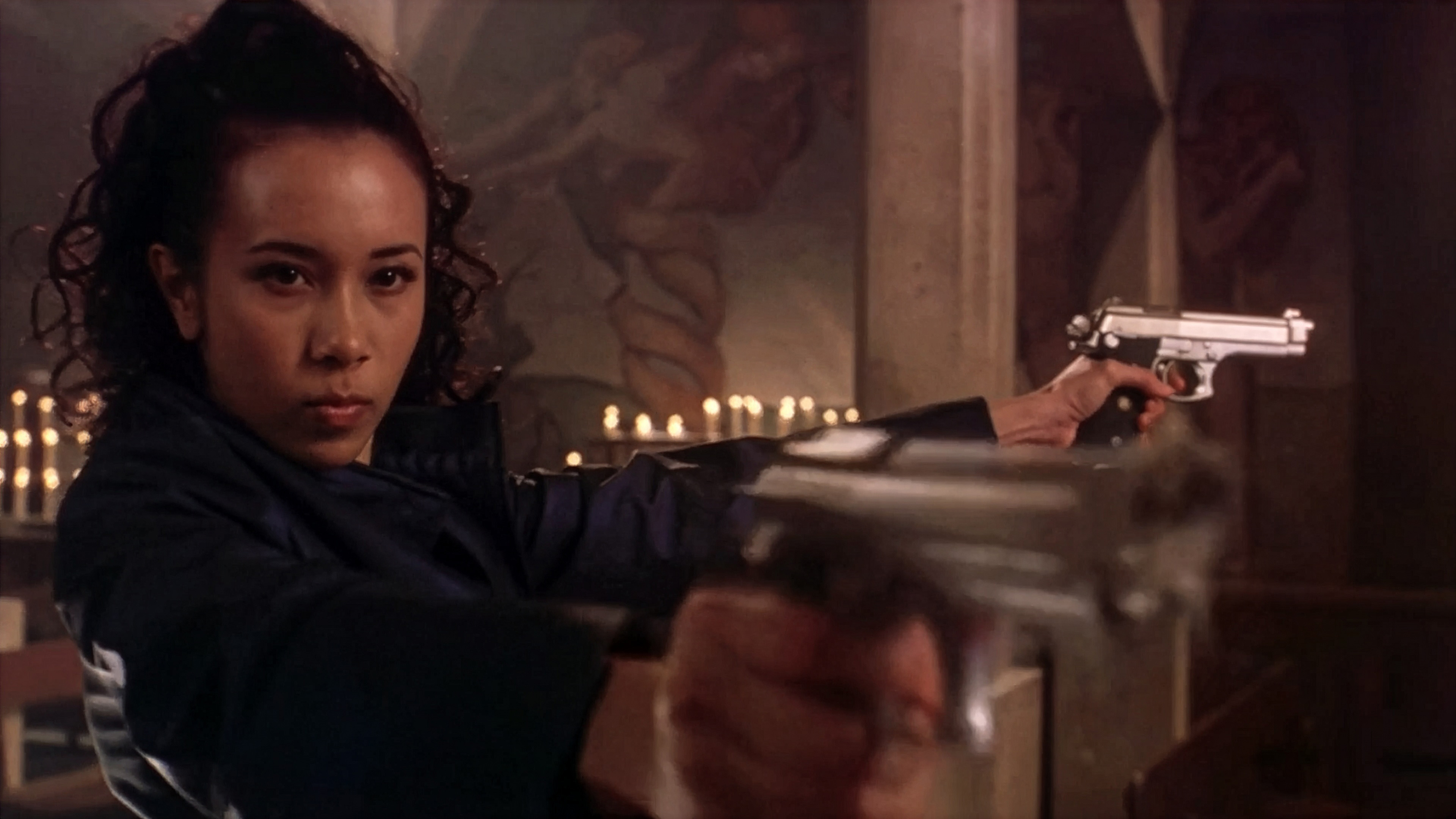 An upscaled still from 'King of Comedy' showing Karen Mok as the character Cuckoo To. She is in a candlelit room, looking intensely at the camera while pointing two pistols forward.